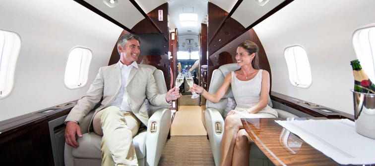 couple clinking champagne glasses smiling on private jet