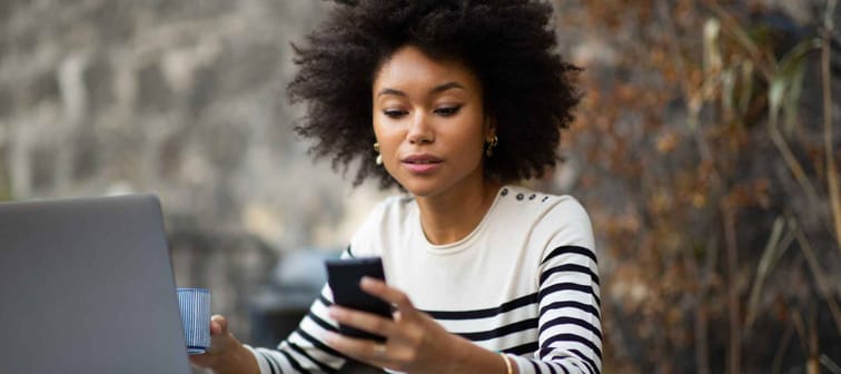 Portrait young african american woman sitting with laptop and using mobile phone