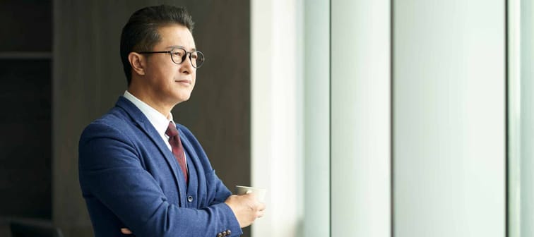 portrait of a asian business leader senior manager standing by window thinking