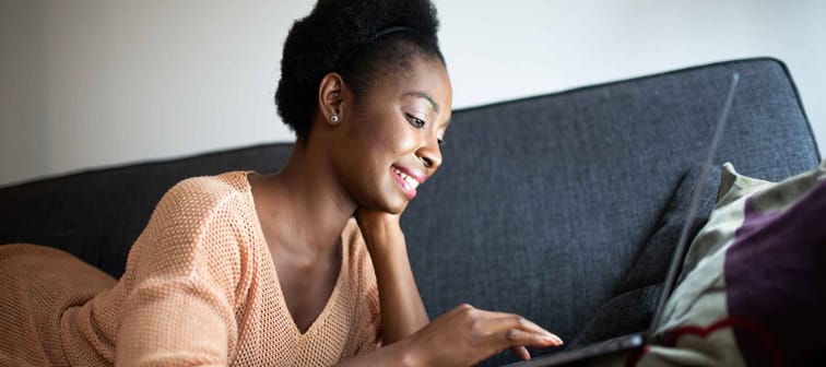 Close up portrait smiling young black woman lying on sofa with laptop computer