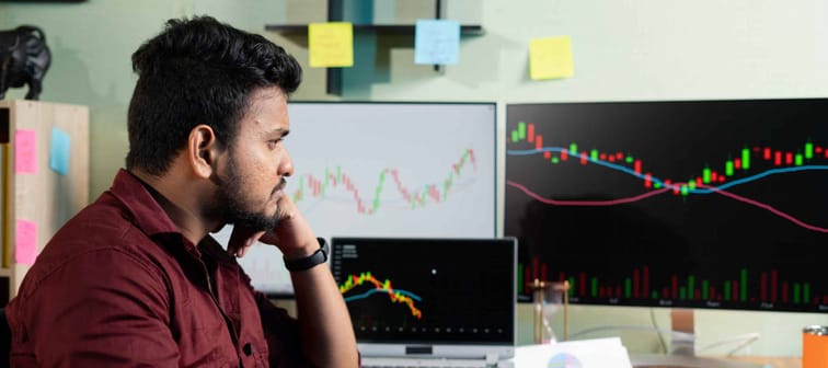 Thinking Young man while trading in front of stock market charts on monitor - concept of risk in investing money on equity shares and disappointed about market crash.