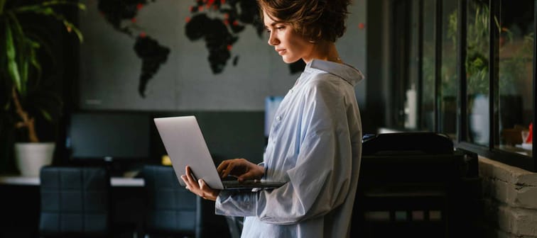 Beautiful young concentrated business woman wearing shirt using laptop while standing in modern workspace