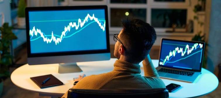 Crypto trader investor analyst looking at computer screen analyzing financial chart data on pc and laptop monitor
