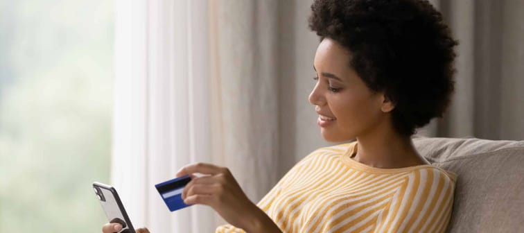 Happy young African American woman holding cellphone and bank credit card in hands