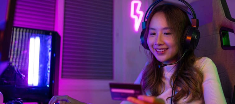 Gamer girl with neon light background, dark room, smiling at credit card with headphones on. cryptocurreny and gaming