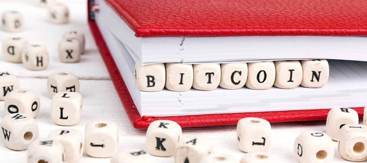 Word Bitcoin written in wooden blocks in red notebook on white wooden table. Wooden abc.