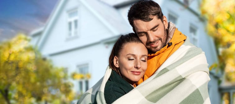 couple embracing wrapped in a blanket in front of a house