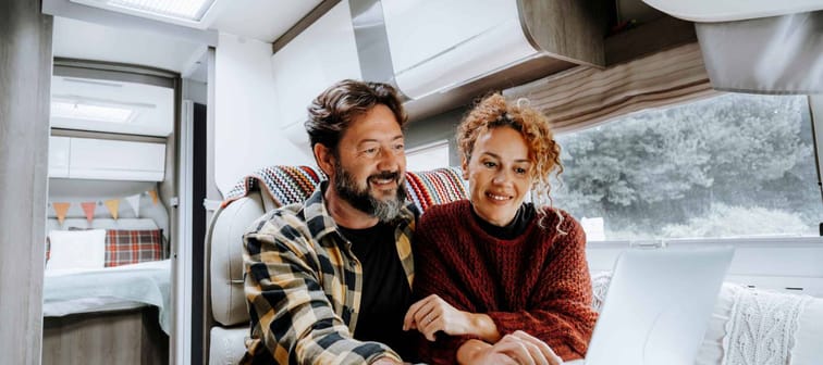 Happy travel couple lifestyle smile and use laptop together inside a modern camper van in vanlife offgrid alternative office workplace.