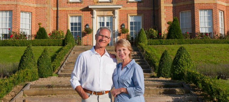 Wide shot of a elderly couple standing together in front of a luxurious estate.
