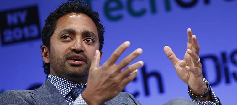 Chamath Palihapitiya sits on stage at a conference, in the middle of speaking with his hands up, gesturing.