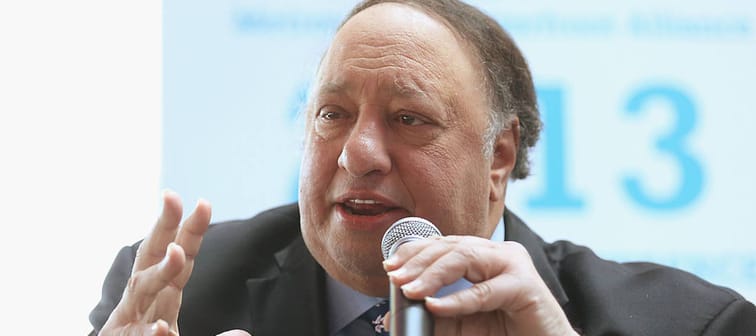 John Catsimatidis speaks at a political forum with a microphone in his hand, the other held up in a gesture.