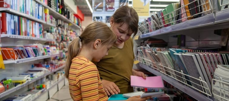 Two young girls buying school supplies in store.