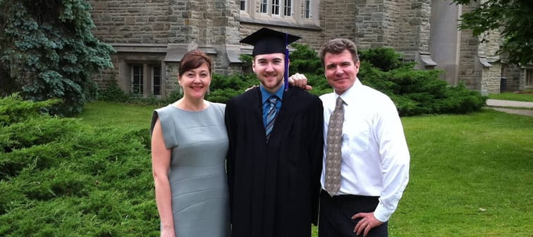 Graduate stands with cap and gown and his parents flanking him.