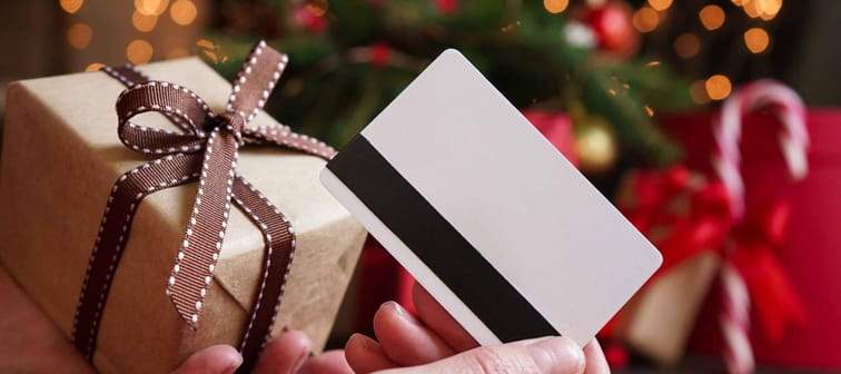 Young woman holding a credit card and a gift box against the background of Christmas decor and gifts, close-up. Christmas and New Year shopping on the Internet, payment by credit card.
