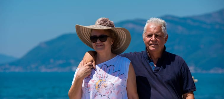 Happy older couple pose for the camera with stunning vacation view behind them.
