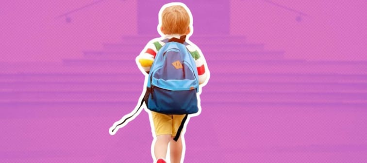 a little boy with his back facing the camera, walking towards a set of school doors