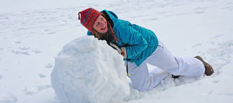 Young college-age woman rolling giant snowball to make snowman.