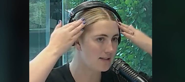 Woman in a radio studio talking with headphones on.