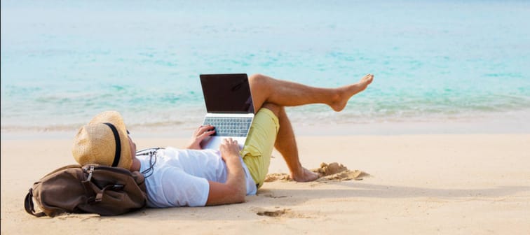 Man working on laptop computer while relaxing on the beach.