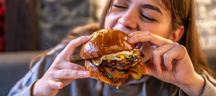 A woman eats a big, appetizing burger.