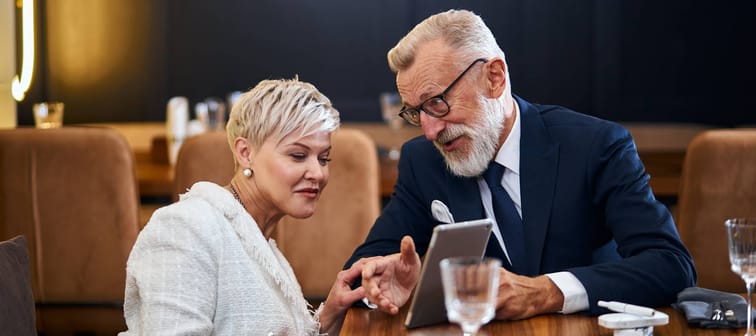 Older Man smiles and shows woman tablet screen during dinner date.