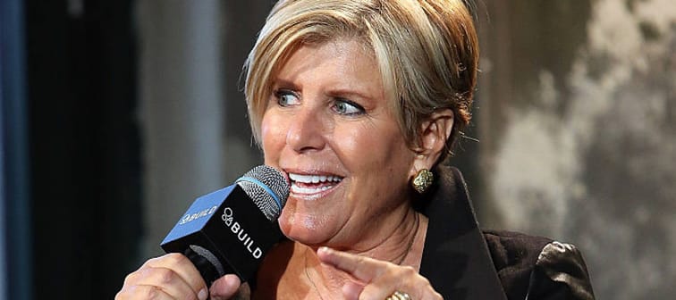 Suze Orman dressed in black, sitting on stage and talking forcefully into a microphone,
