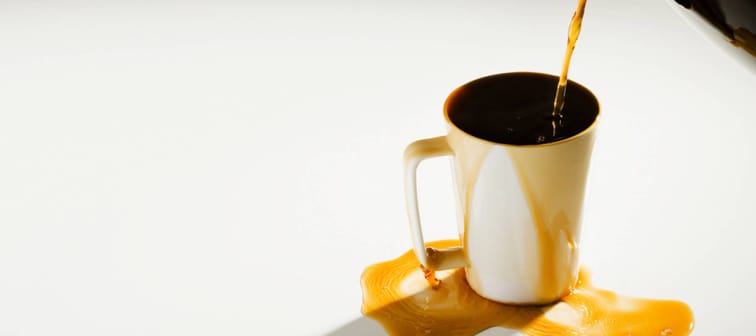 coffee being poured into an overflowing mug against a white backdrop