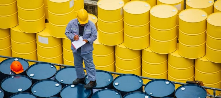 man making notes wearing construction hat and standing on oil drums