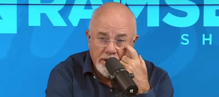 Dave Ramsey seen on set of his radio show, scratching his eye and looking puzzled.