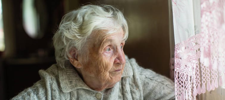 An elderly old woman looks sadly out the window. Care for lonely pensioners.