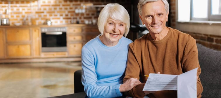 Happy relationships. Joyful positive elderly couple sitting together and smiling while checking the bills