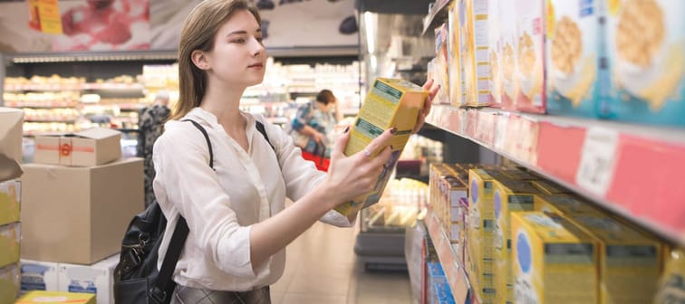Woman buys quick breakfasts at a supermarket. Girl isa in the store with a box of flakes and hands. Woman chooses the products in the supermarket.