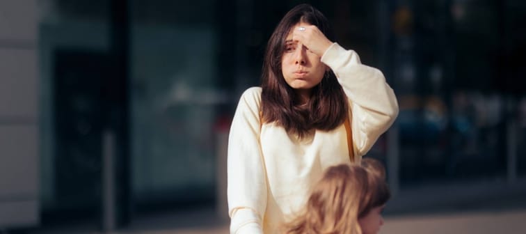 stressed mom pushing a shopping cart with her daughter in a parking lot