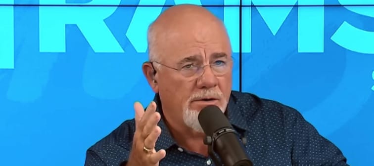 Dave Ramsey on set of his radio show, looking concerned and holding one hand up.