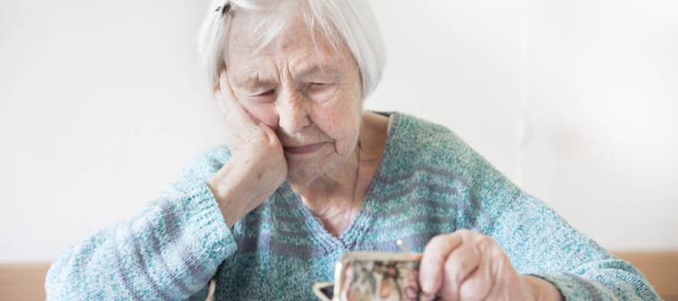 elderly 96 years old woman sitting at table at home and counting remaining coins from pension in her wallet