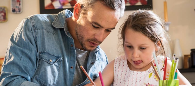 A father helps his little daughter to do her homework for the school.