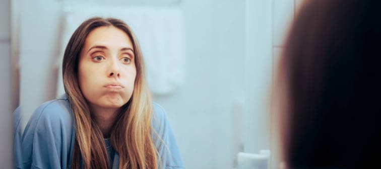 unhappy Caucasian woman looking in the mirror, feeling overwhelmed