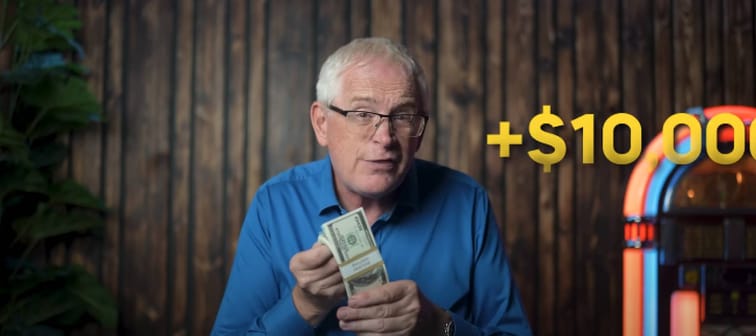 Older man holds up stack of US bills, fanning it out.