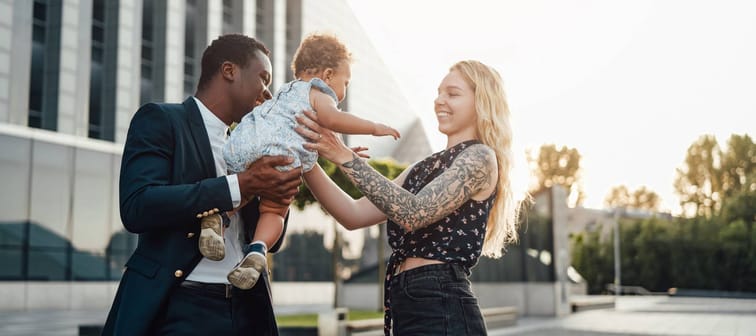 Shot of happy mixed family of father giving his daughter to his wife outside.