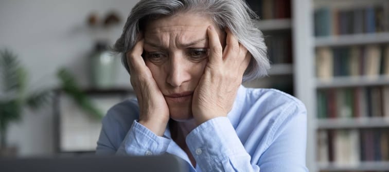 Frustrated senior retired woman touching head, looking at laptop screen with despair,