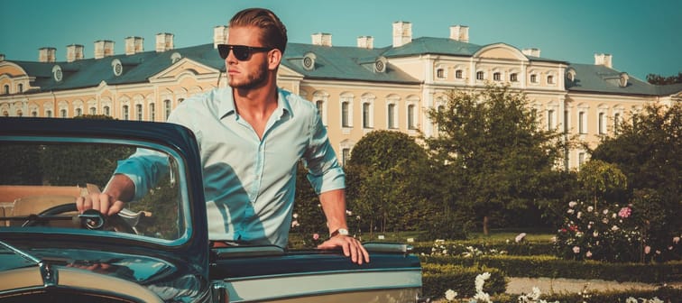 Confident wealthy young man with briefcase near classic convertible