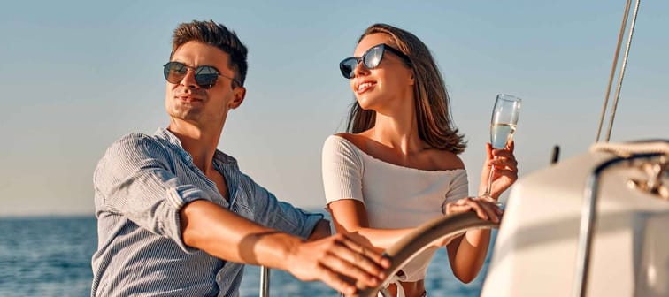 Group of friends relaxing on luxury yacht. Having fun together while sailing in the sea. Romantic couple sitting near steering wheel. Traveling and yachting concept.