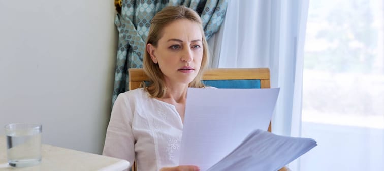 Sad emotion on face of mature woman reading paper letter, contract, document. Upset female sitting at home on chair