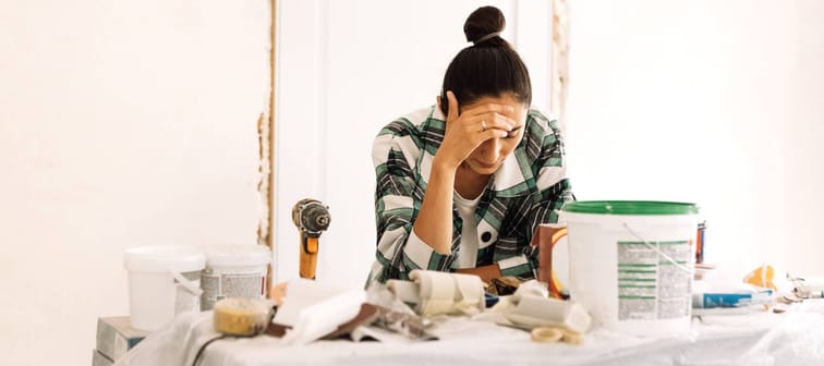 A young attractive woman is standing among building materials and inventory. A charming girl in casual clothes is thinking about doing house repairs. Apartment renovation.