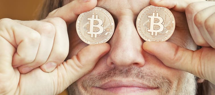 Bearded man holding symbolic bitcoins over his eyes