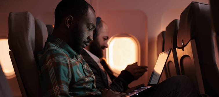 Businessmen work on their wireless devices during a flight.