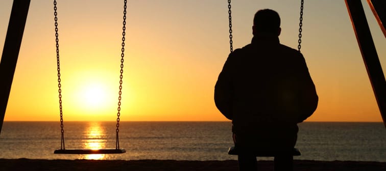 Back view backlighting silhouette of a man sitting on swing alone