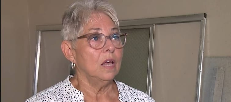 Older woman with short grey hair speaks to camera.