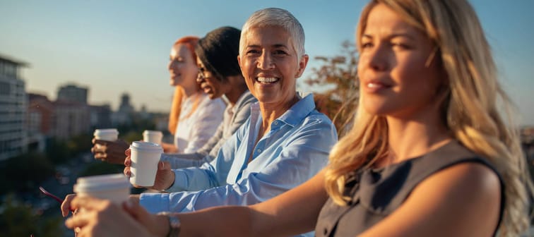 Women enjoying coffee from a balcony.