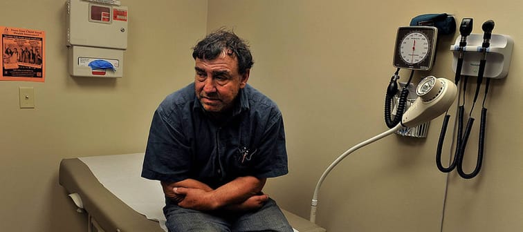 Man sits in doctor's office at end of examination table, looking uncomfortable and uncertain.